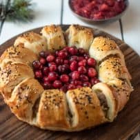 Puff pastry rolled into a wreath shape filled with pork sausage on a board with fresh cranberries in the center