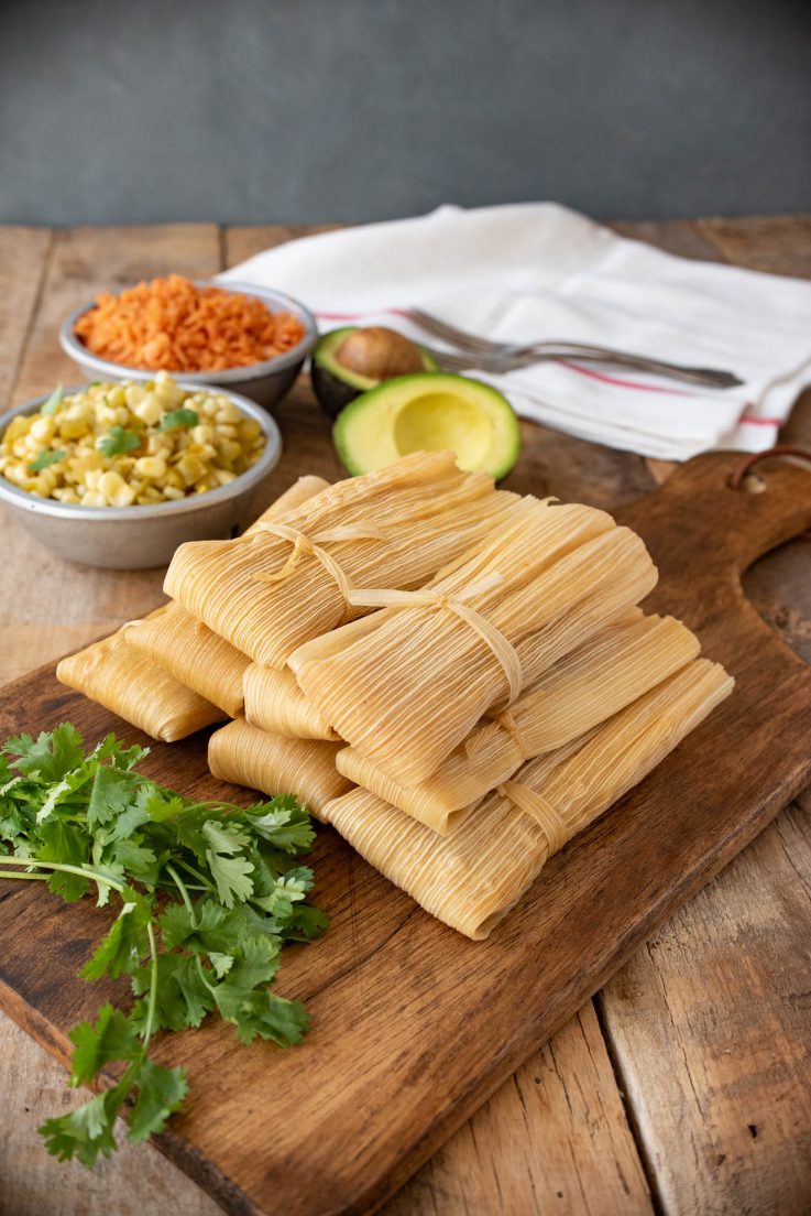 Tamales wrapped in corn husks piled onto a serving board