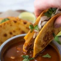 Shredded beef quesabirria taco being dipped in chile sauce