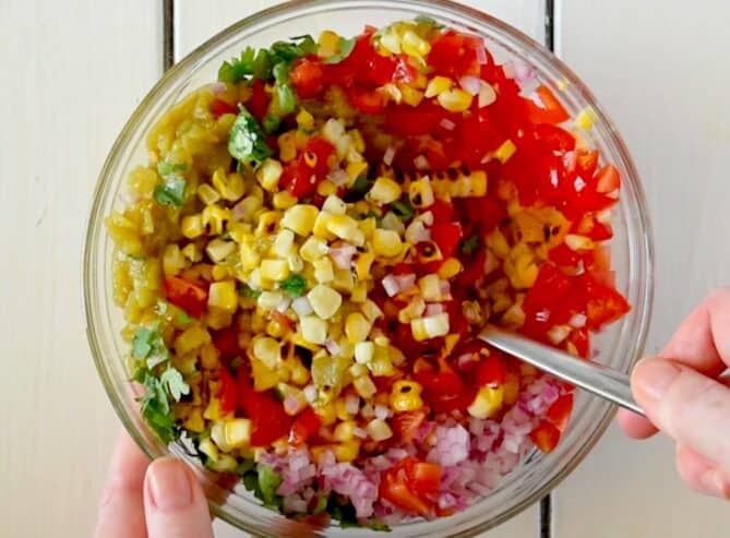 Mixing corn, tomato, red onion and cilantro in a bowl with a spoon
