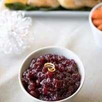 Cranberry sauce garnished with an orange rind in a white serving bowl with a turkey in the background