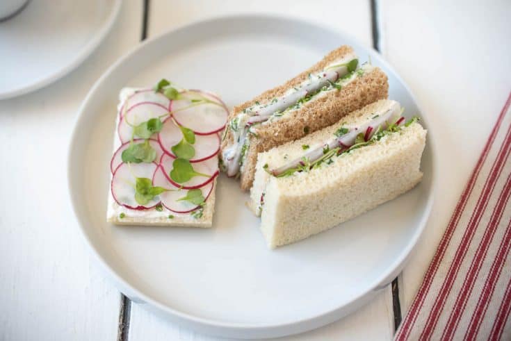 An open faced and mini crustless radish and herb butter sandwiches on a white plate