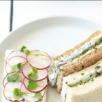 On the left of a plate is an open-faced radish and herb butter sandwich and on the right, 2 crustless sandwiches