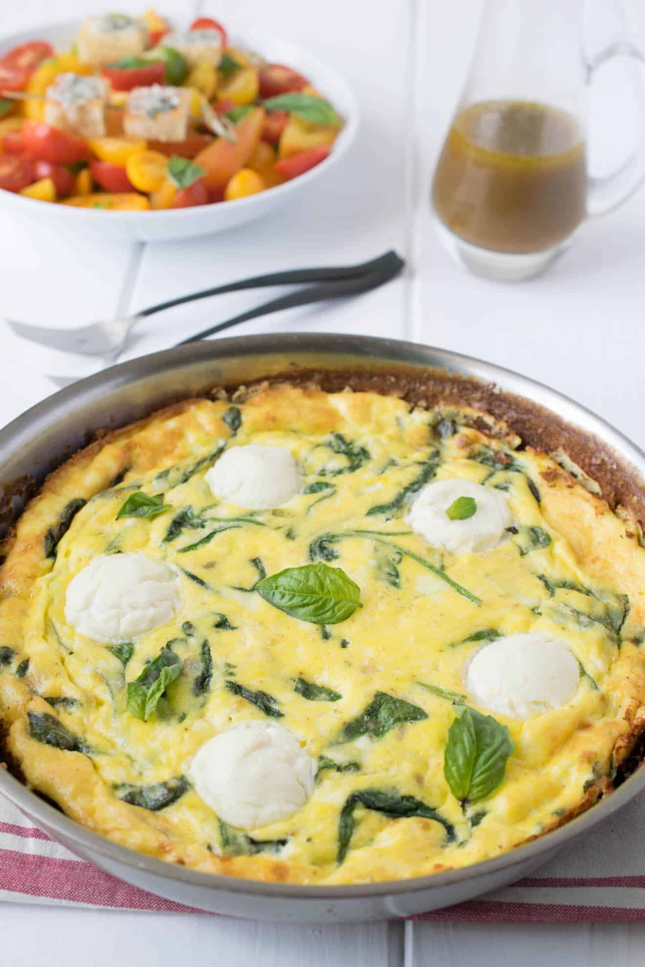 Frittata in a pan topped with fresh ricotta, green spinach and basil