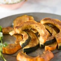 Slices of orange and green skinned acorn squash on a pewter plate