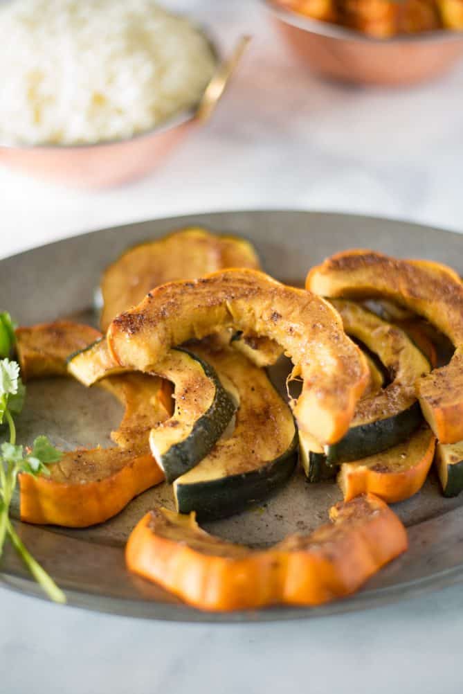 Slices of orange and green skinned acorn squash on a pewter plate