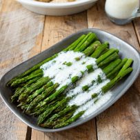 Asparagus spears on a grey plate drizzled with lemon ricotta sauce