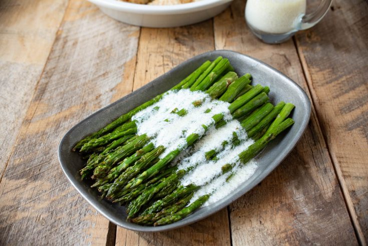 Asparagus spears on a grey plate drizzled with lemon ricotta sauce