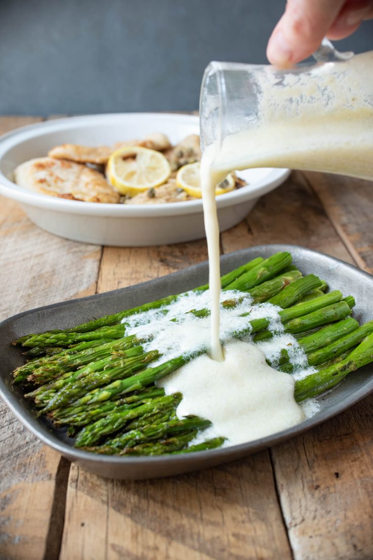 Pouring lemon ricotta sauce over roasted asparagus