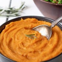 A closeup of roasted carrot and parsnip puree garnished with rosemary sprigs