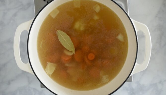 Vegetable stock, vegetables and a bay leaf cooking in a pan.
