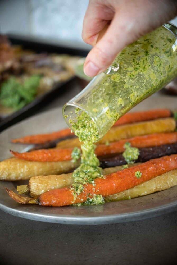 Pouring green pesto over roasted carrots