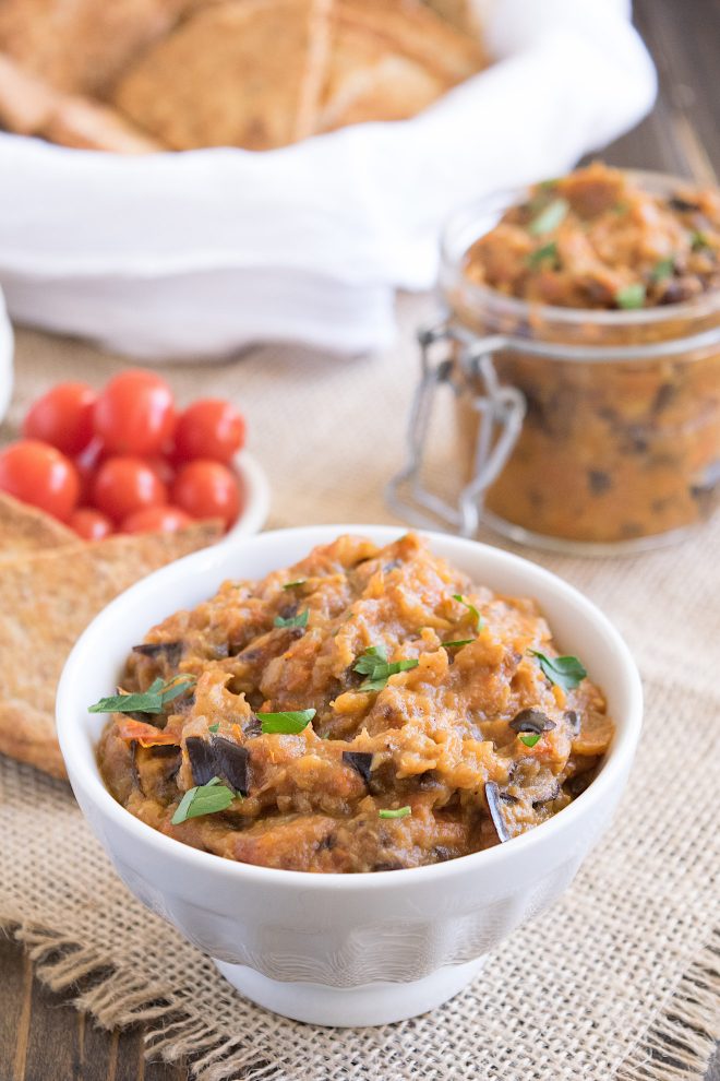 A white bowl filled with eggplant dip with cherry tomatoes