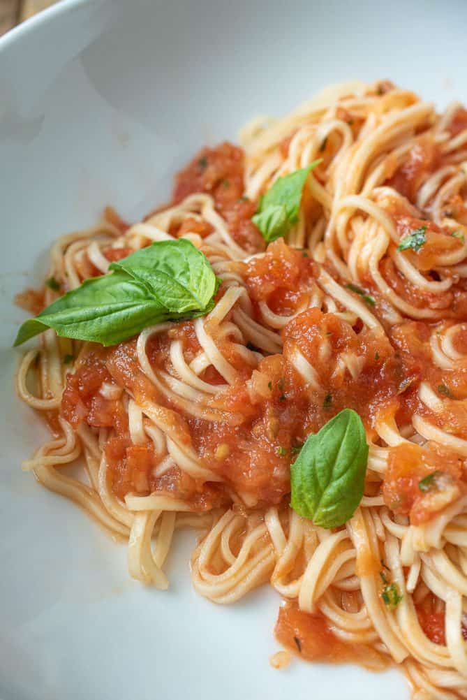 A closeup of roasted tomato sauce mixed with fresh linguine garnished with fresh basil leaves