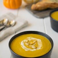 A round black bowl filled with roasted pumpkin and root vegetable soup garnished with a swirl of sour cream and roasted pumpkin seeds