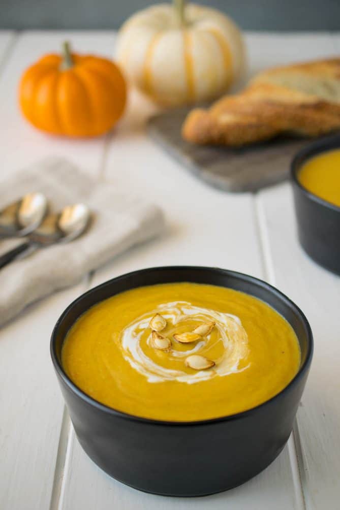 A round black bowl filled with roasted pumpkin and root vegetable soup garnished with a swirl of sour cream and roasted pumpkin seeds