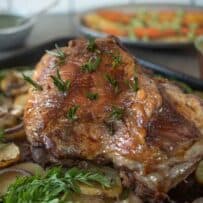 A perfectly browned, roasted leg of lamb in a roasting pan surrounded by vegetables