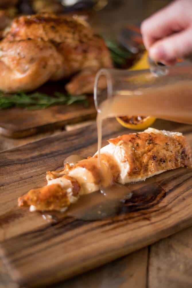 Sliced chicken on a board pouring gravy on top
