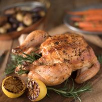 A whole roasted chicken on a cutting board with lemon halves