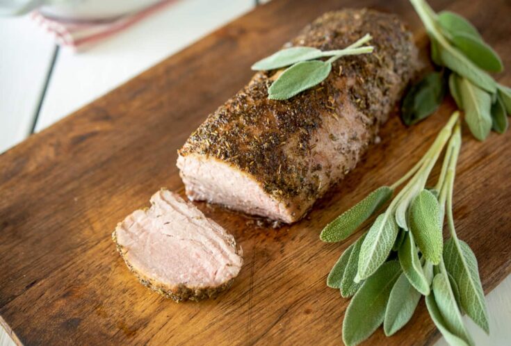 A closeup of sliced pork tenderloin surrounded by fresh sage leaves