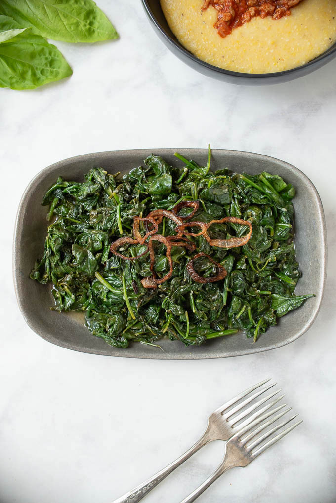 Vibrant green sauteed spinach from above with rings of crispy shallots