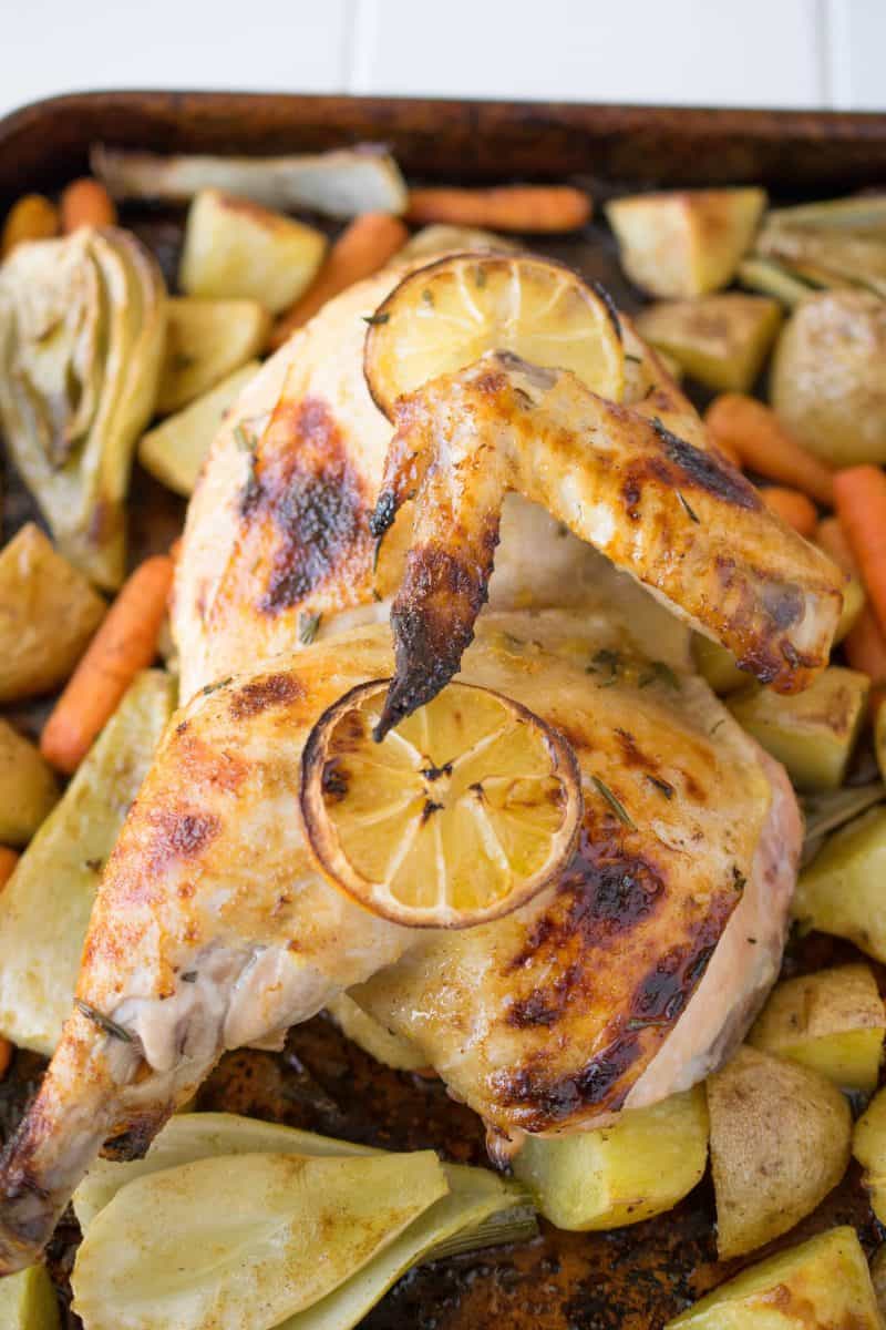 Half of a roasted chicken on a baking sheet of vegetables