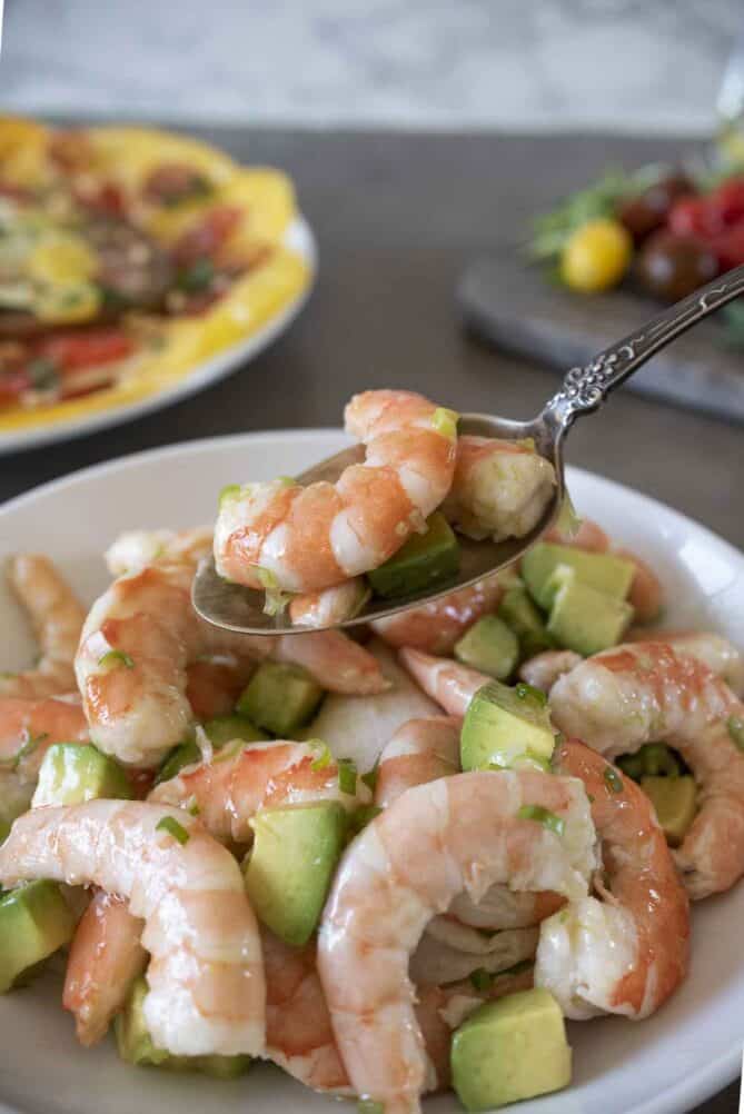 A spoon holding a shrimp and some avocado