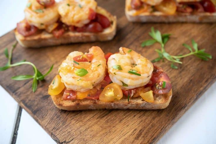 2 cooked shrimp on top of chopped tomatoes on a slice of crispy bread