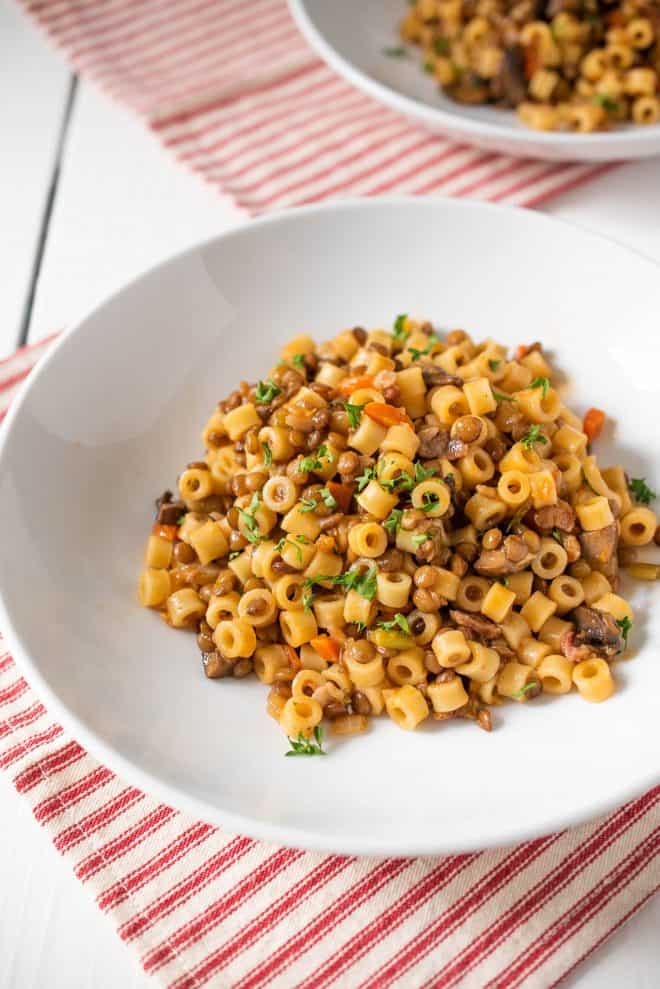 A closeup showing the round ditalini pasta mixed with the lentil sauce served on a white plate