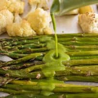 Drizzling a green herb sauce over fresh roasted asparagus and cauliflower