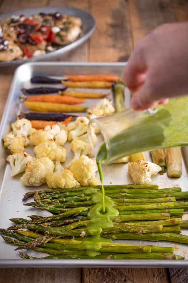 Pouring herb sauce over roasted asparagus for Healthy New Year Meal Ideas
