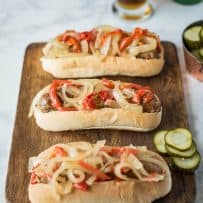 3 bratwurst sandwiches on a board with pickles