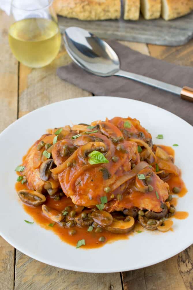 A large white plate of chicken and a tomato sauce with mushrooms