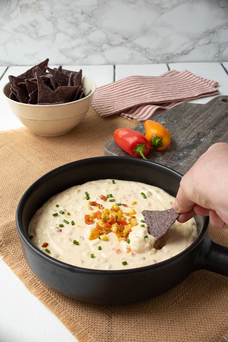 Corn and pepper cheese dip in a black bowl dipping a blue corn tortilla