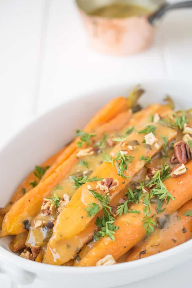 A closeup of orange honey glazed carrots topped with herbs and nuts