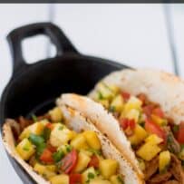 A closeup of pineapple chunks with tomato and cilantro on top of carnitas pork tacos