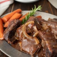 Short ribs and gravy on a plate with carrots and rosemary