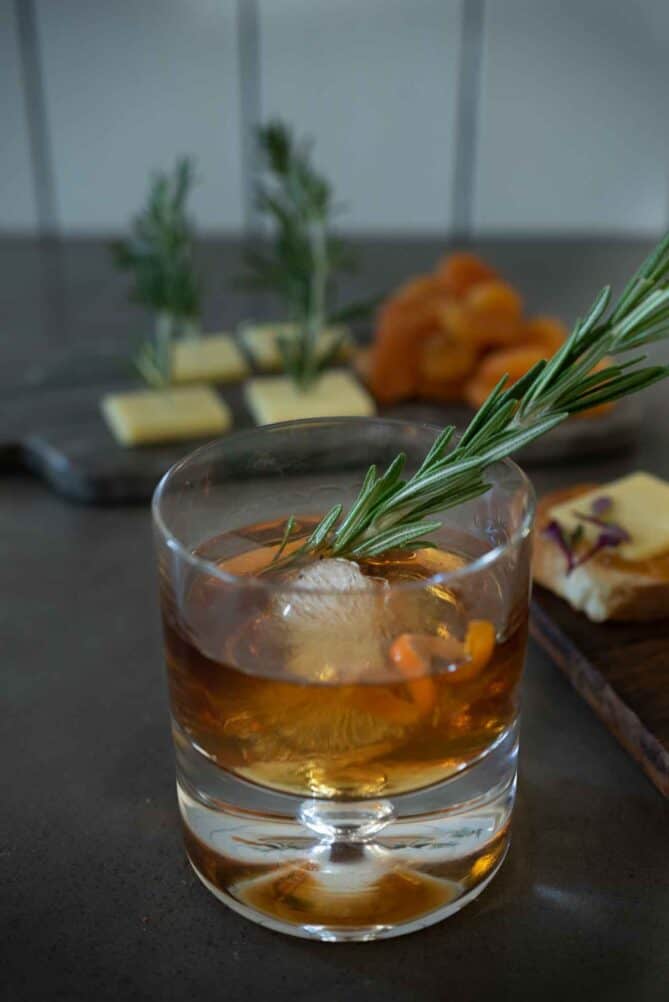 A dark brown cocktail in a short glass with a large ice ball