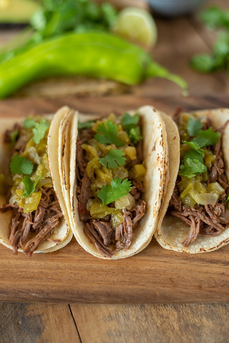 3 Sonoran shredded beef tacos on a board with hatch chile sauce and cilantro