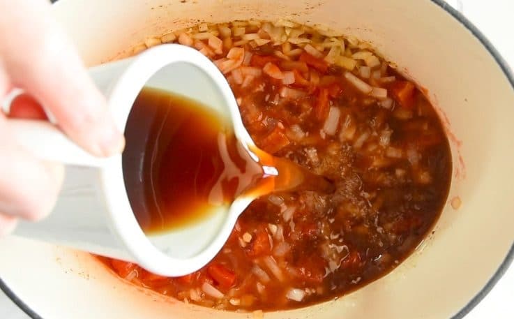 Beef stock being poured into the pan with onions, garlic and tomatoes