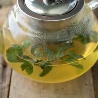 A closeup of soothing therapeutic herbal tea in a glass teapot with fresh herbs