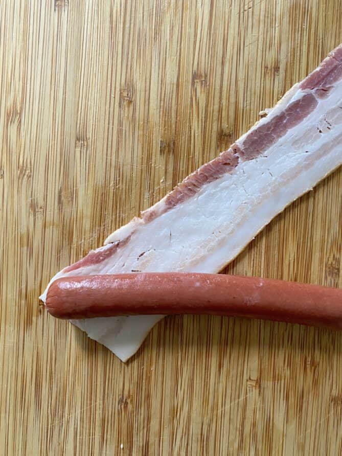 Wrapping a hot dog in a slice of bacon