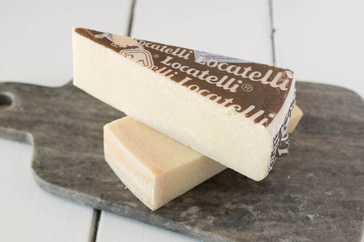 A wedge of Parmesan and pecorino romano cheeses on a grey board