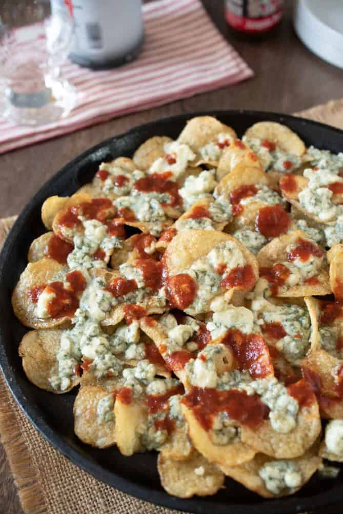A closeup of potato chips with melted blue cheese and hot sauce