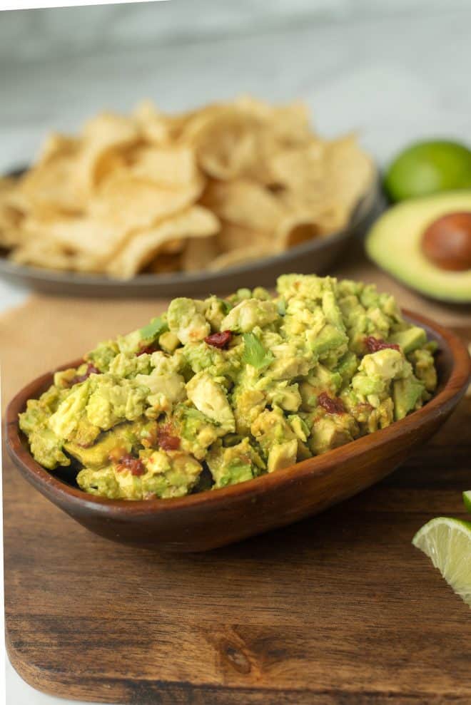 Chunky spicy guacamole in a wooden bowl with tortilla chips