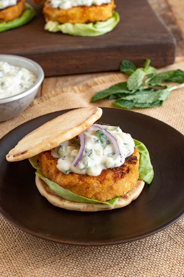 Spicy curry veggie burger on naan bread with lettuce, raita and red onion on a dark plate