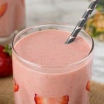 A pretty pink smoothie in a glass with a straw and fresh strawberries