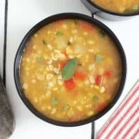 A bowl of sweet corn sage soup garnished with a sage leaf served with bread