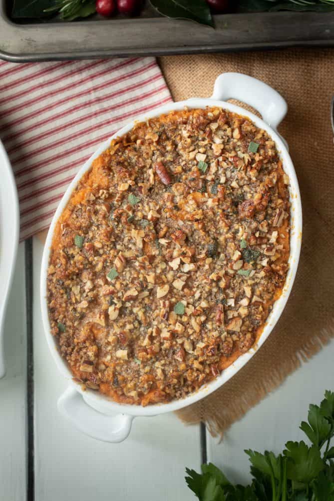 From overhead, an oval baking pan of sweet potato casserole topped with a crumbled pecan topping with butter and sage
