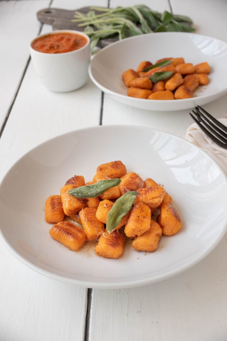 2 white bowls of sweet potato gnocchi garnished with crispy sage